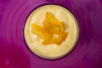 Top down view on delicious yellow dessert with fruit pieces surrounded by purple from table or plate