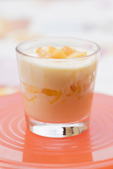 Close up on side of creamy yellow dessert stuffed with fruit slices in clear glass over red plate