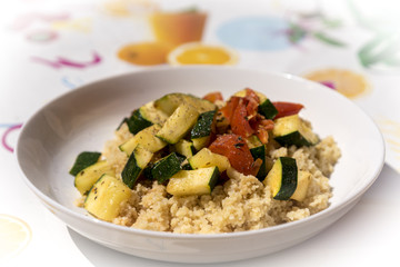 Close up on small plate full of cooked couscous with zucchini and tomato slices