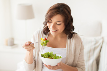 smiling young woman eating salad at home