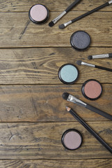 Aerial view of individual eye shadows and make up brushes arranged on a rustic wooden background to form a page border