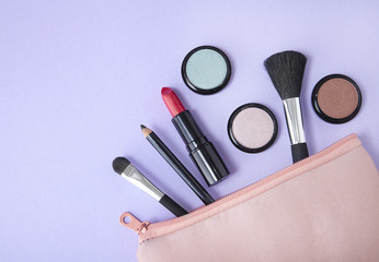 A make up pouch with cosmetic products spilling out on to a pastel purple background, forming a page border