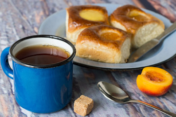 Breakfast.   Freshly baked buns with apricot jam on an old metallic a plate and a mug of of tea on a wooden table.