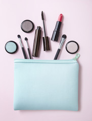 Aerial view of a make up bag with cosmetic products spilling out on to a pastel pink background