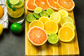 A bottle of lemonade and citrus slices on a cutting board on a black wooden background, selective focus