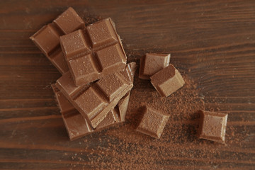 Chocolate pieces covered with cocoa powder on wooden background