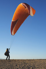 Back view of professional paraglider on ground with flying bright parachute in blue sky