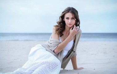 Beautiful woman in a white dress on the ocean coast. Happy girl on the beach, the wind fluttering hair. Beach vacation.