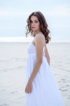 Beautiful woman in a white dress on the ocean coast. Happy girl on the beach, the wind fluttering hair. Beach vacation.