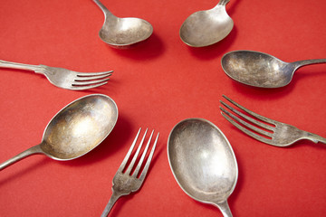 Antique silver cutlery arranged in a circle on a red background