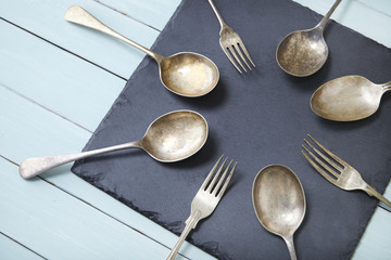 Old silver cutlery arranged in a circle on a slate and wooden table background