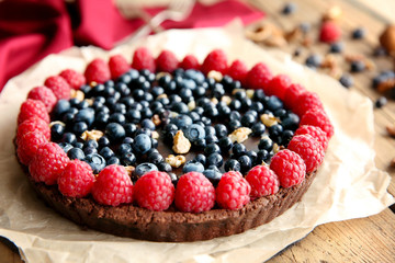 Delicious chocolate tart with berries and nuts on paper, closeup