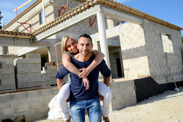 cheerful young happy couple in love in front of contruction site of their new house