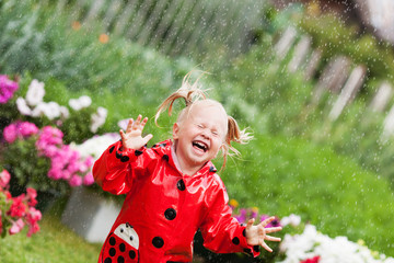 Happy fun pretty little girl in red raincoat with umbrella walking in park summer