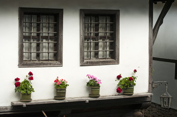 Fototapeta na wymiar Wooden windows of old village house wall with pots of flowers at front