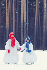 Happy brother and sister in costumes snowman walking in winter forest,