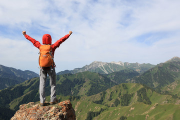 Obraz premium cheering young woman backpacker open arms on mountain peak cliff