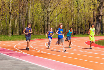 Five running teenage athletes in the stadium
