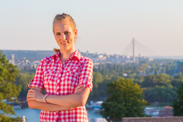Fototapeta premium Portrait of beautiful young female on hill with city in the background during the sunny summer day