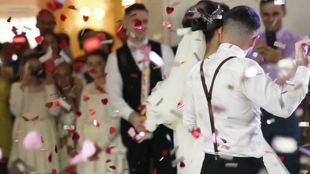 Beautiful brunette bride and handsome groom dancing first dance at the wedding party. Confetti in the air. Very tender moment