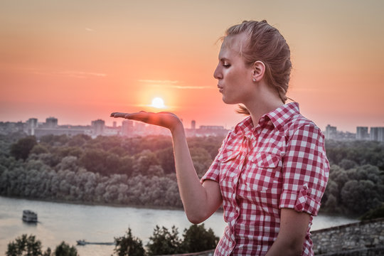 HDR image of female blowing sun from her hand at sunset over city. 