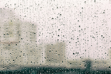 Raining season, abstract raindrop on glass window with city building background, vintage tone