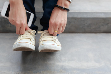 Close up young girl tying shoe laces while sitting on stairs, Urban women fashion lifestyle
