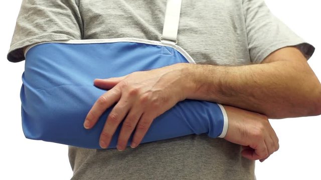 Anonymous man isolated on a white background wearing an orthopedic arm sling rubs his arm after a painful fracture or surgery or other medical incident.