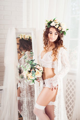 sexy caucasian bride standing in front of the full-length mirror, dressed in white nighty, wreath, with bouquet of flowers, vertical