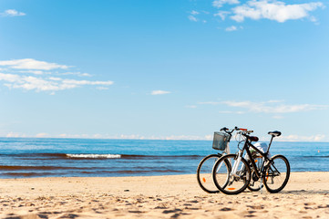 Fototapeta premium Two bicycles standing on the beach sand with blue cloudy sky bac