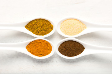 spices (allspice, turmeric, garlic powder, curry) in white spoons, overhead view