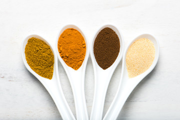 variety of spices (allspice, turmeric, garlic powder, curry) in white spoons, overhead view