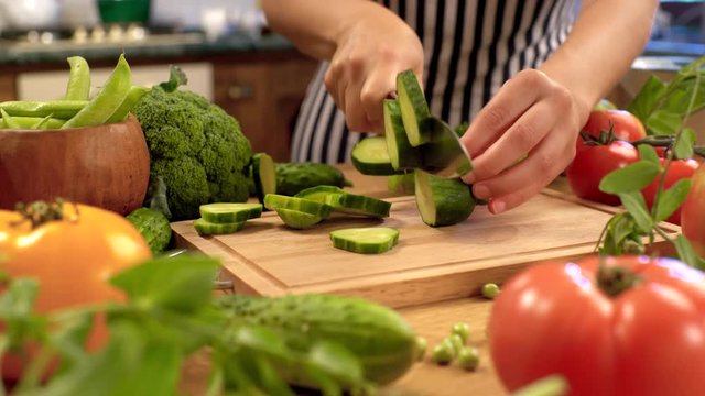 Girl cuts green cucumber. Light board surrounded by fresh 