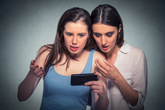 Two surprised girls looking at cell phone discussing latest gossip news