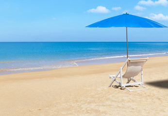 white wooden beach chair and blue parasol on tropical beach in sunny day.