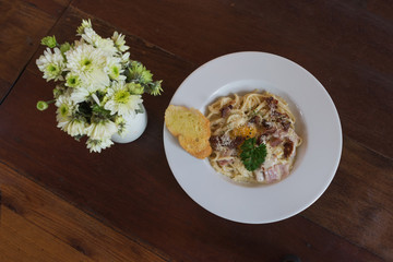 spaghetti carbonara with ham cheese bacon and egg on wooden table and whit cream flower ready to eat