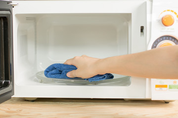 Close up woman hand with microfiber cleaning rag wiping microwave oven.