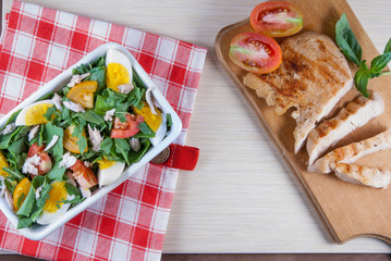 Chicken fillet, grilled, with a large portion of salad with fresh vegetables and herbs on a wooden table with a red cloth into a cell. top view