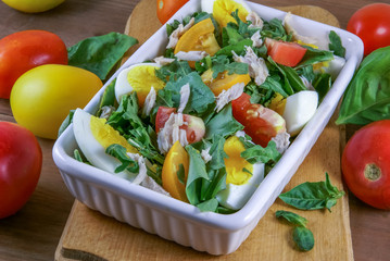 A large portion of salad with fresh basil leaves, arugula, parsley, tomatoes. On a wooden table with a tablecloth. 