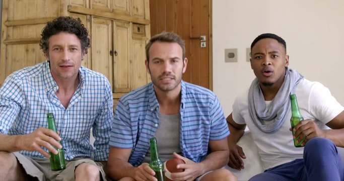 Friends drinking a beer and watching american football match on the television at home 