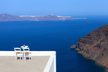 Perfect relaxing balcony with two wooden chairs overlooking Santorini's bay