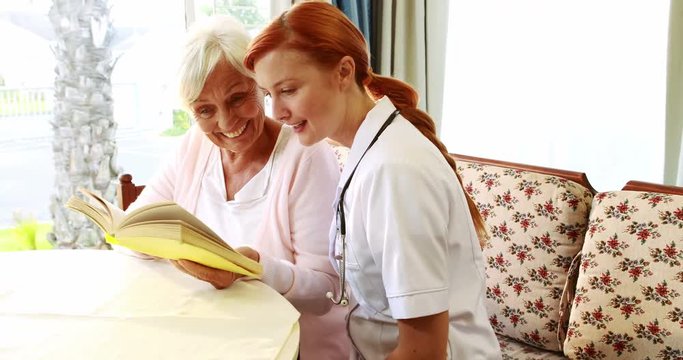Nurse and old woman reading book together in retired home