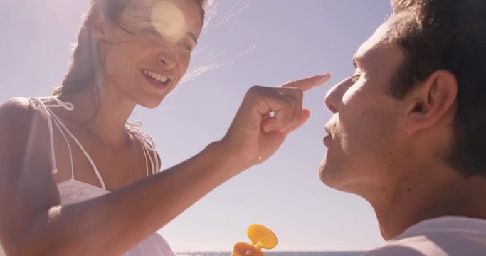 Woman putting sunscreen to her boyfriend at the beach
