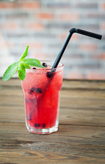 Red refreshing lemonade with berries and ice on a wooden background. Summer drink