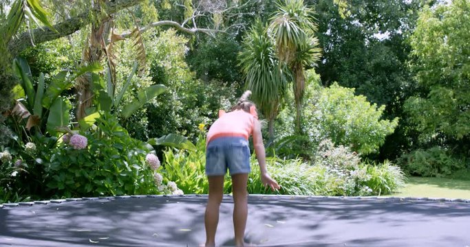 Blonde girl doing back flip on trampoline in the garden