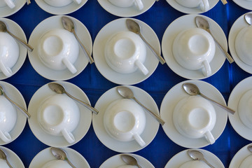 Rows of clean white upside down cups, dish and spoon in a cafeteria or restaurant ready to serve a hot beverage, full frame background