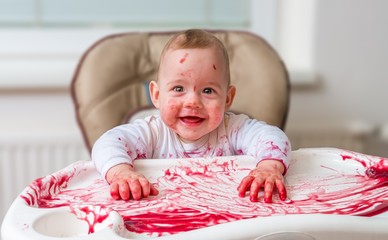 Messy and dirty baby is eating snack with hands.