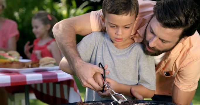 Close up on a father is teaching to his son to do a barbecue in the garden 
