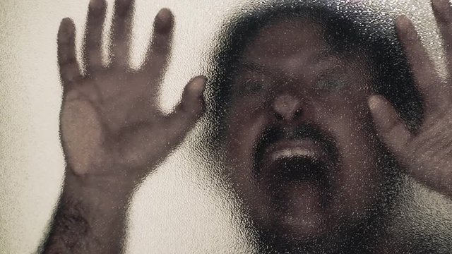 A zombie lurking behind a frosted glass door and attacking the viewer. Horror Halloween themed shot.
