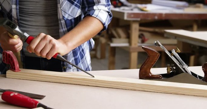 Focus on carpenter using hammer and chisel on wooden plank